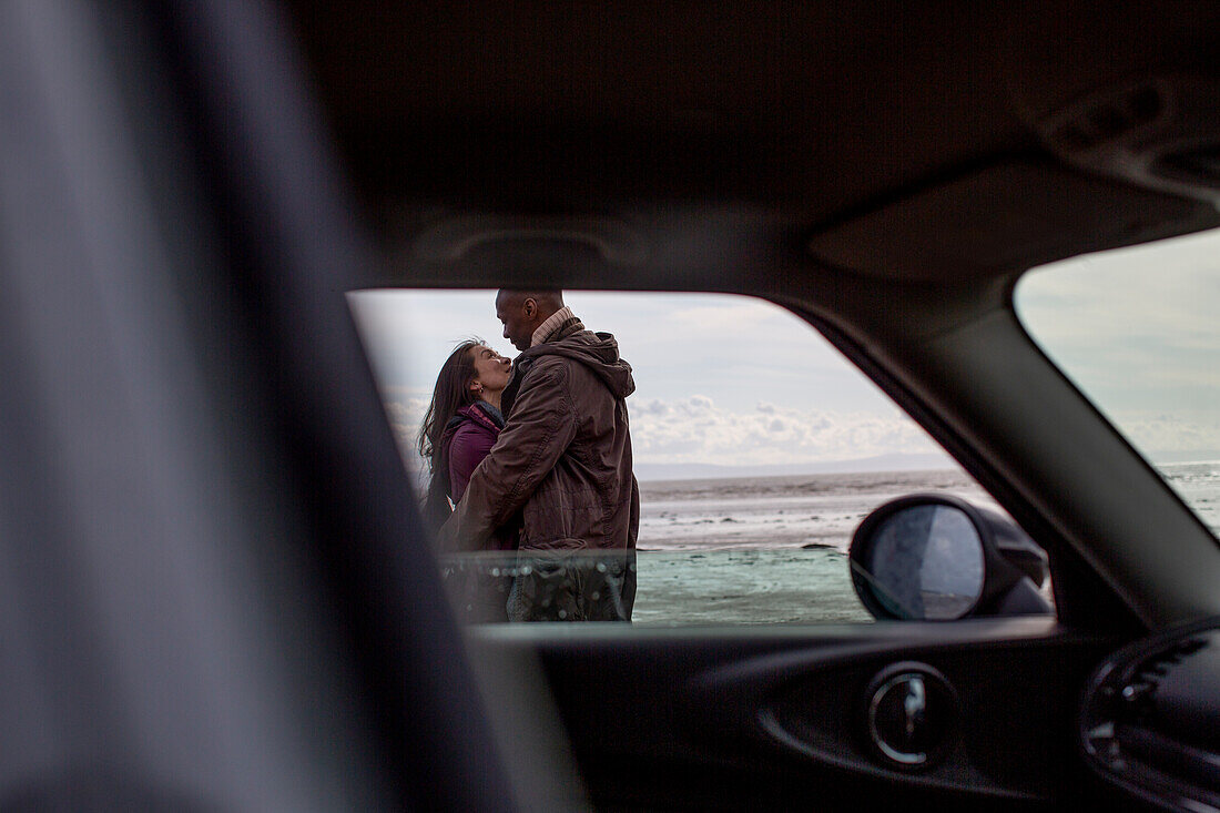 Affectionate couple hugging outside car on beach