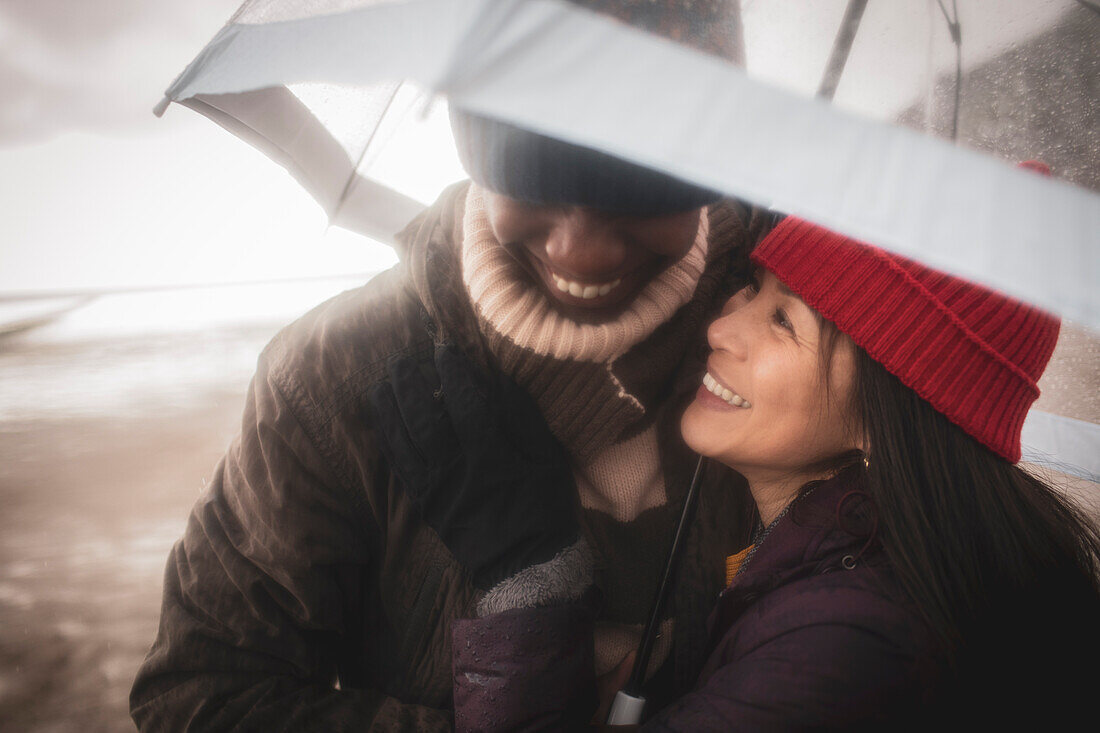 Happy couple under umbrella on wet winter beach