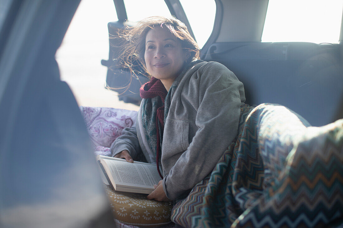 Woman reading book at back of car