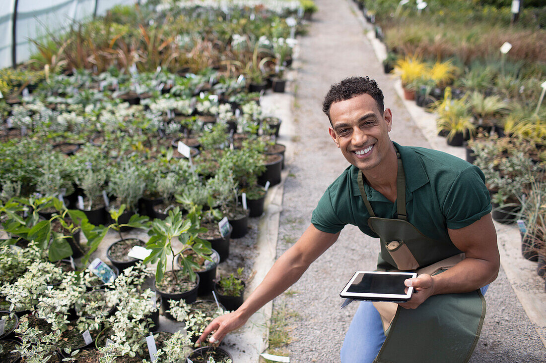 Happy male garden shop owner with digital tablet and plants