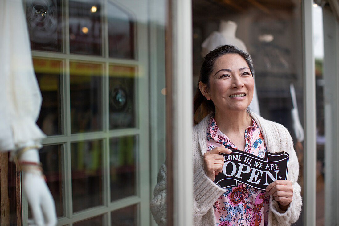 Female shop owner holding open sign outside boutique