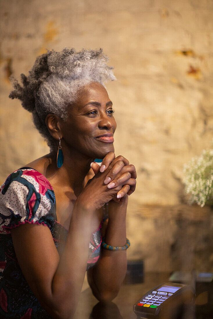 Smiling satisfied senior female shop owner looking away