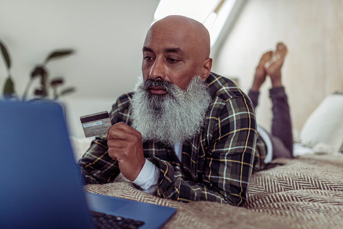Man with beard and credit card shopping online at laptop
