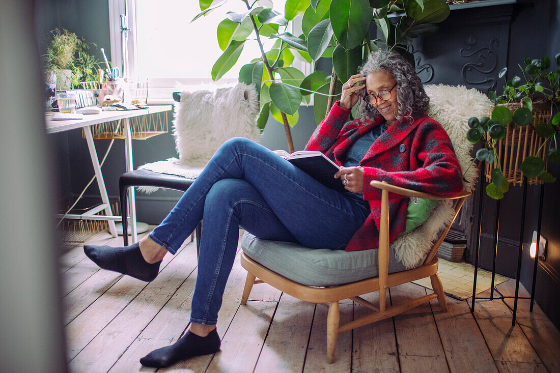 Woman reading book in armchair at home