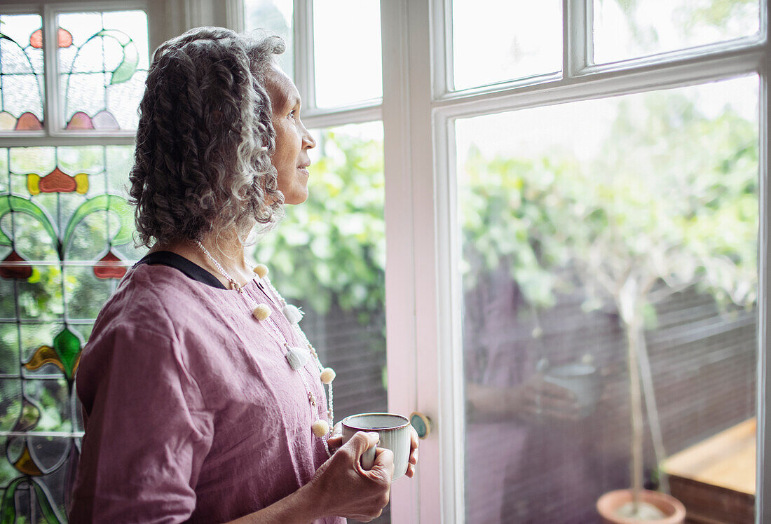 Thoughtful woman drinking tea at window