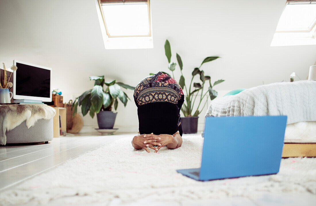 Woman practicing yoga online with laptop on bedroom rug