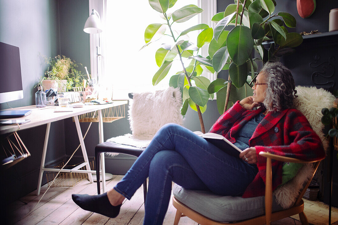 Woman reading book in armchair in home office