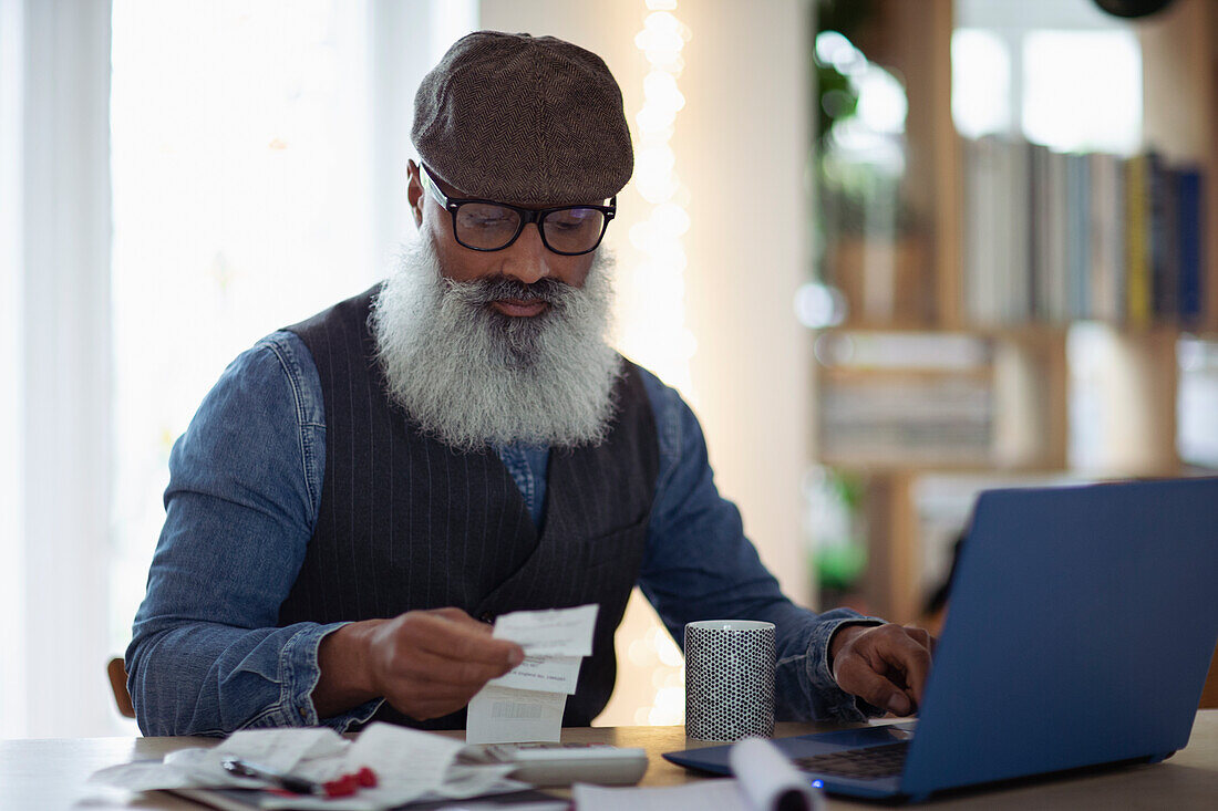 Mature man with beard budgeting at laptop