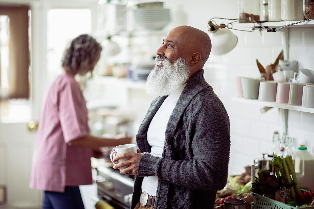 Happy mature man with beard drinking tea in kitchen