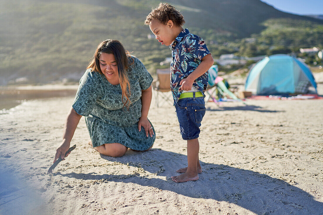 Mother and son with Down Syndrome drawing with stick in sand