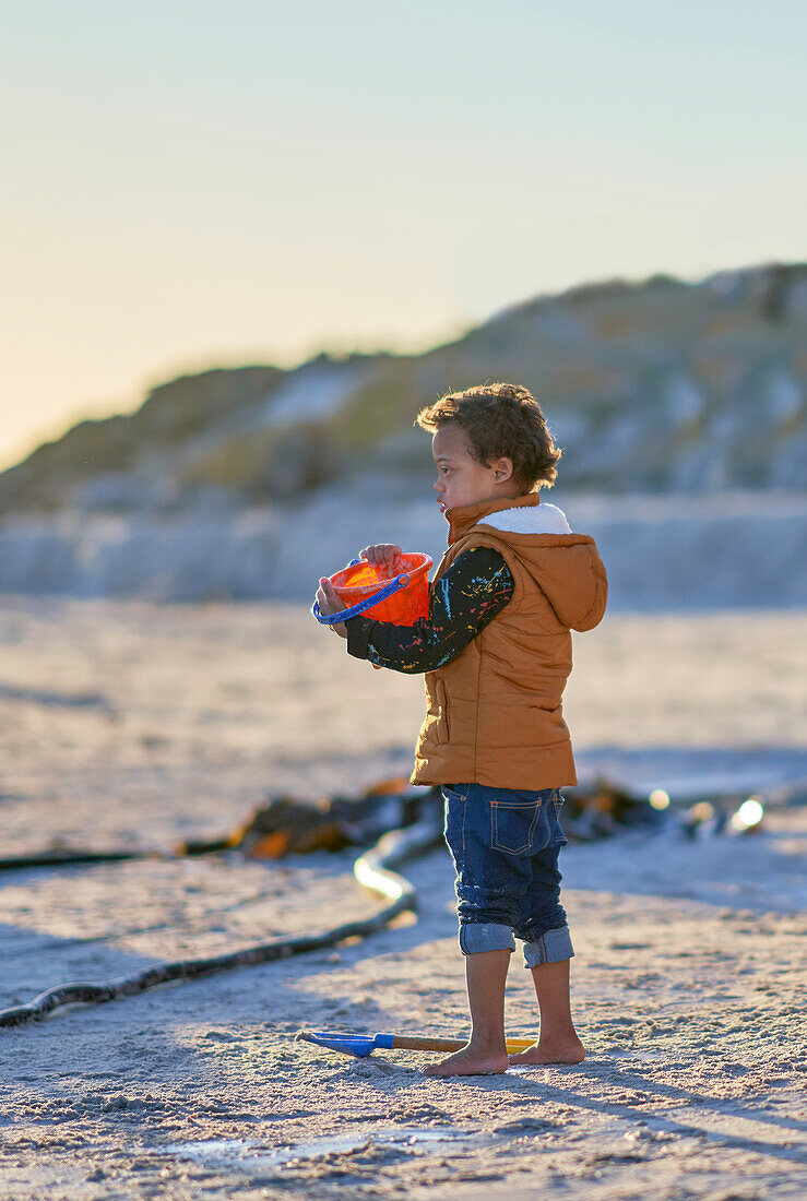 Boy with Down Syndrome holding bucket on sandy beach
