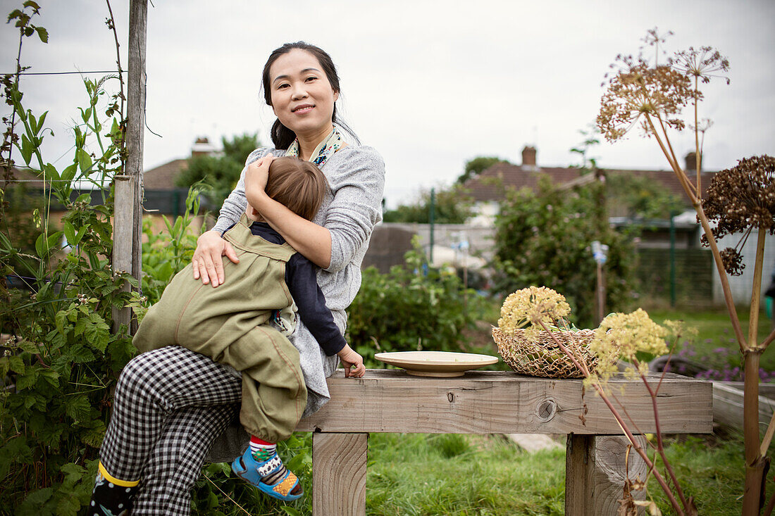 Happy mother holding tired toddler son on garden bench