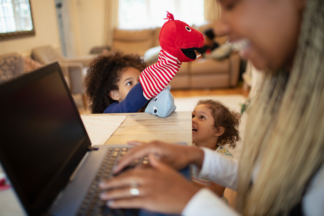 Daughters playing with puppets behind mother working