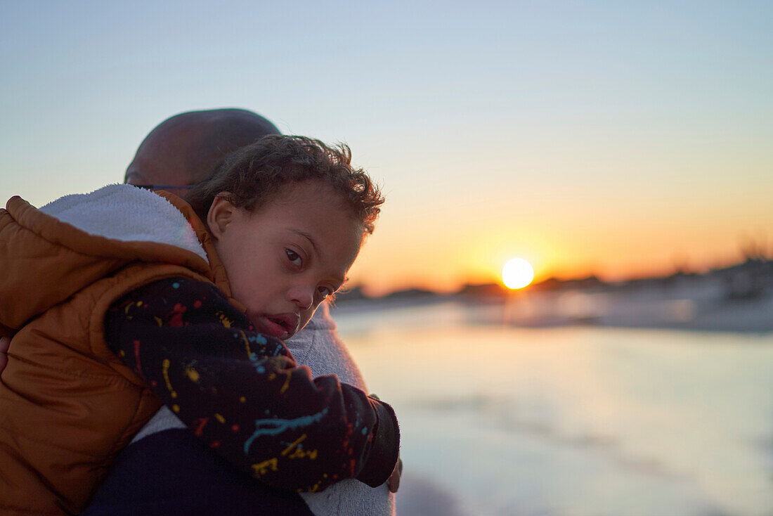Boy with Down Syndrome on father shoulder on beach at sunset
