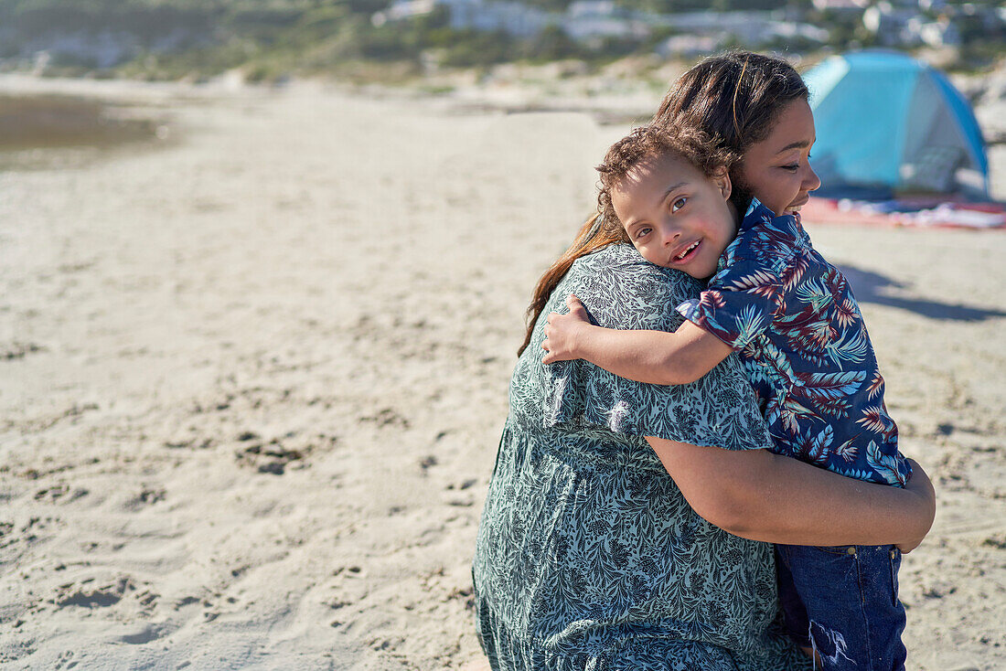 Happy boy with Down Syndrome hugging mother on beach