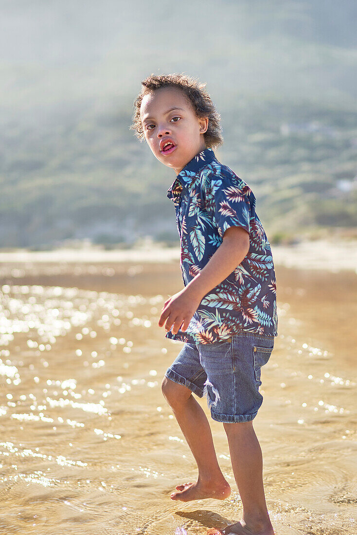 Boy with Down Syndrome wading in ocean on sunny beach