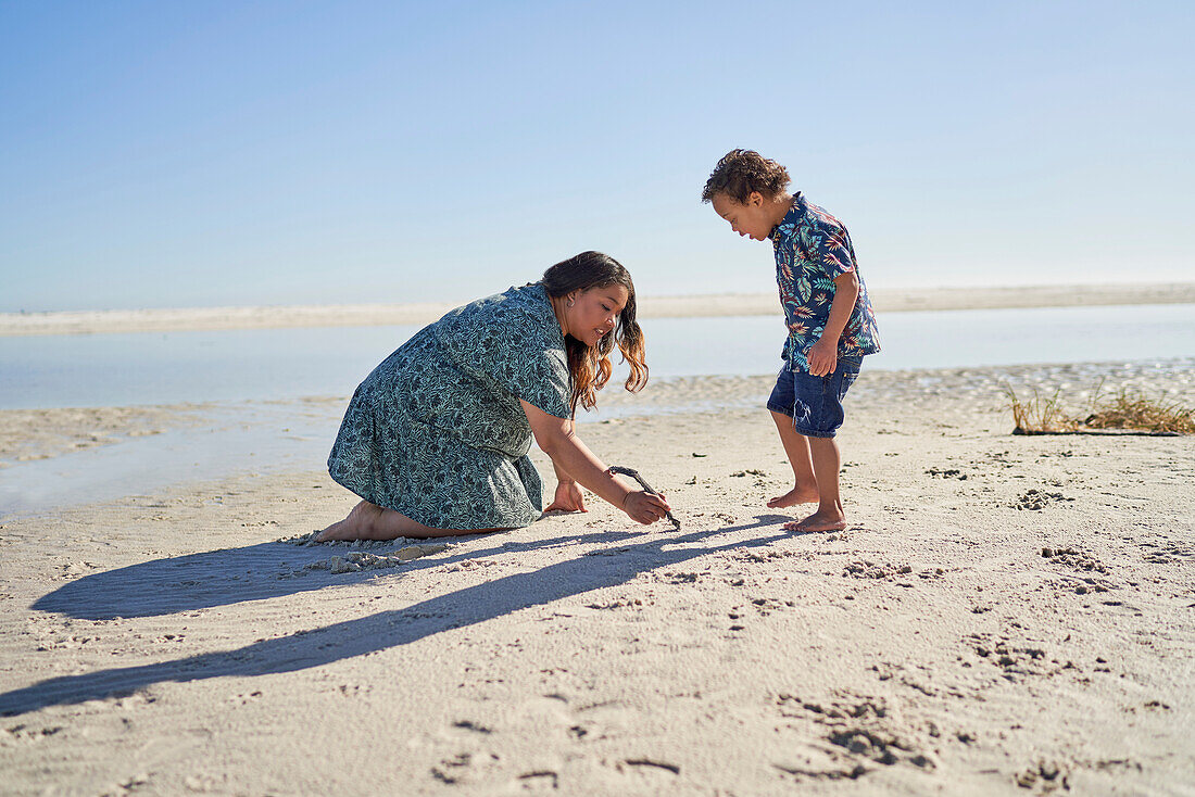 Mother and son with Down Syndrome drawing in sand with stick