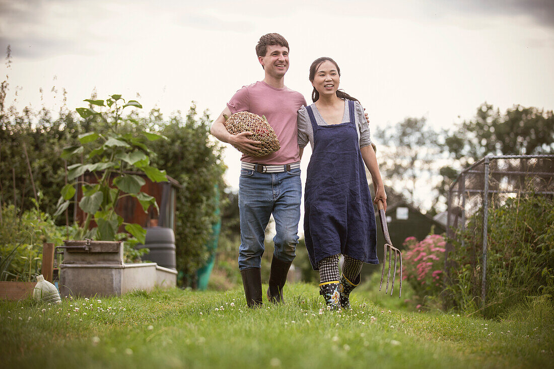 Happy couple walking with vegetables and pitchfork in garden