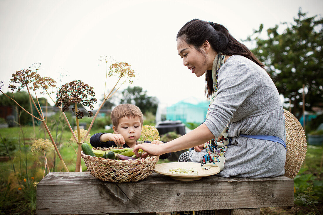 Mother and toddler son with harvested vegetables in garden