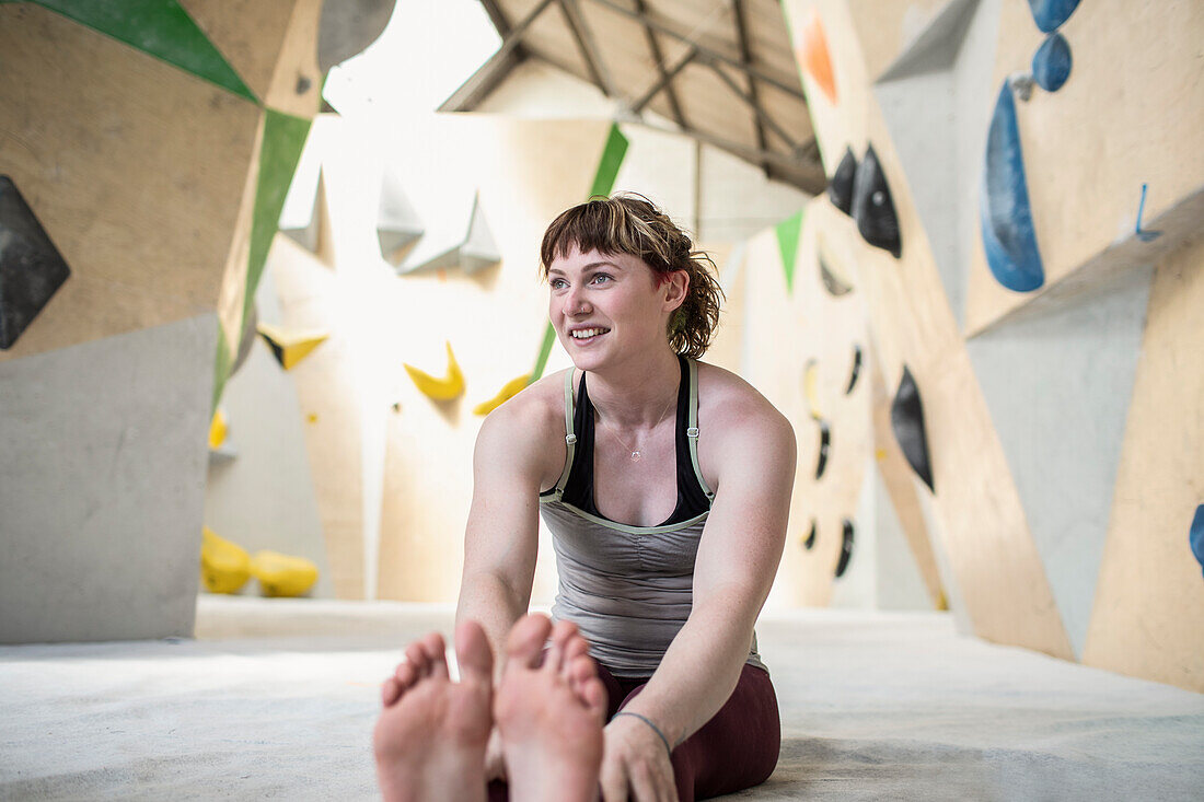 Smiling young woman stretching below climbing wall