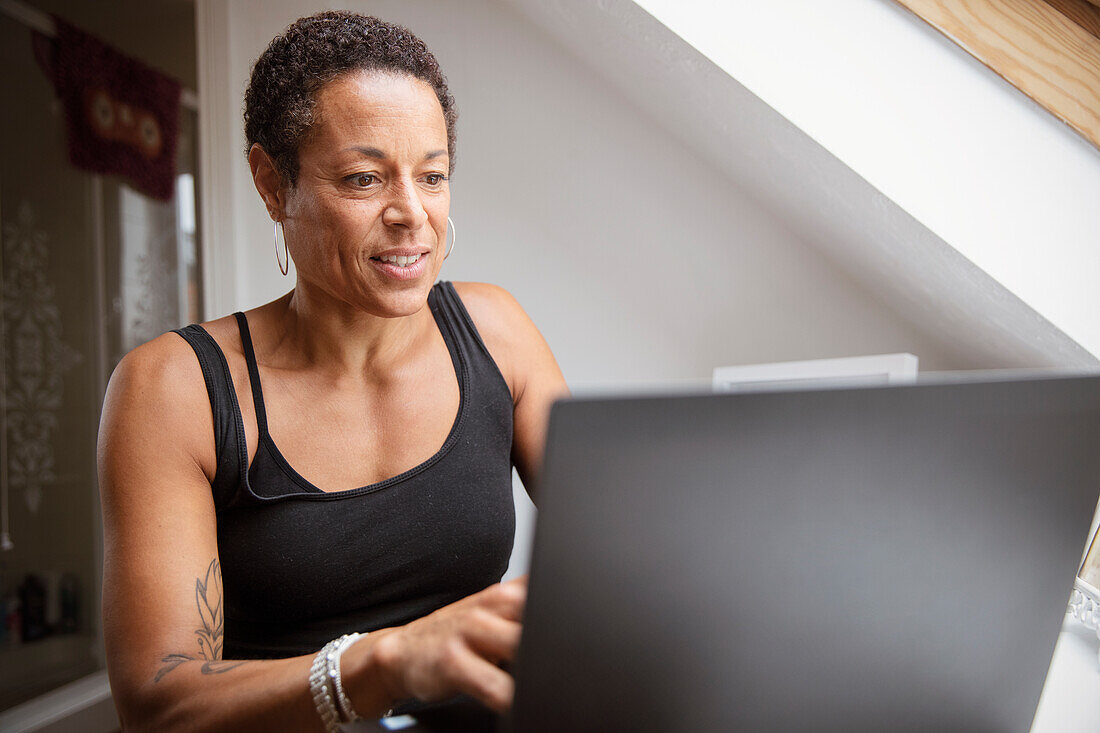 Mature woman in tank top working from home at laptop