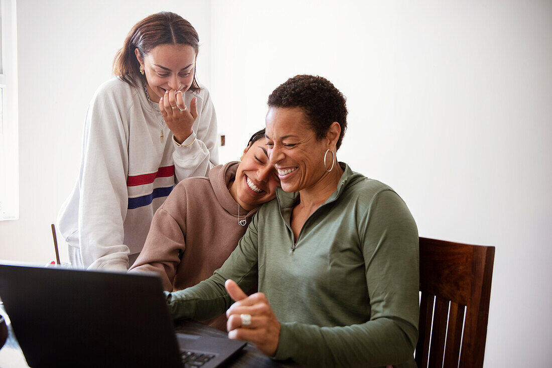 Happy mother and daughters using laptop in dining room