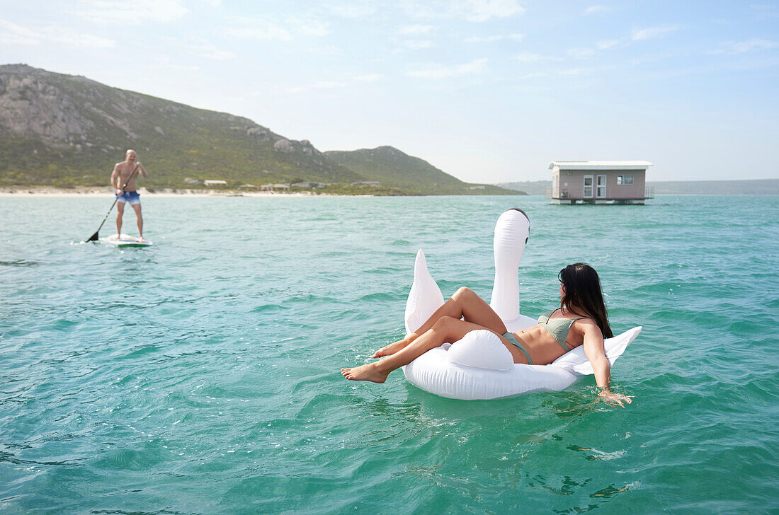 Couple on inflatable swan and paddle board on summer ocean