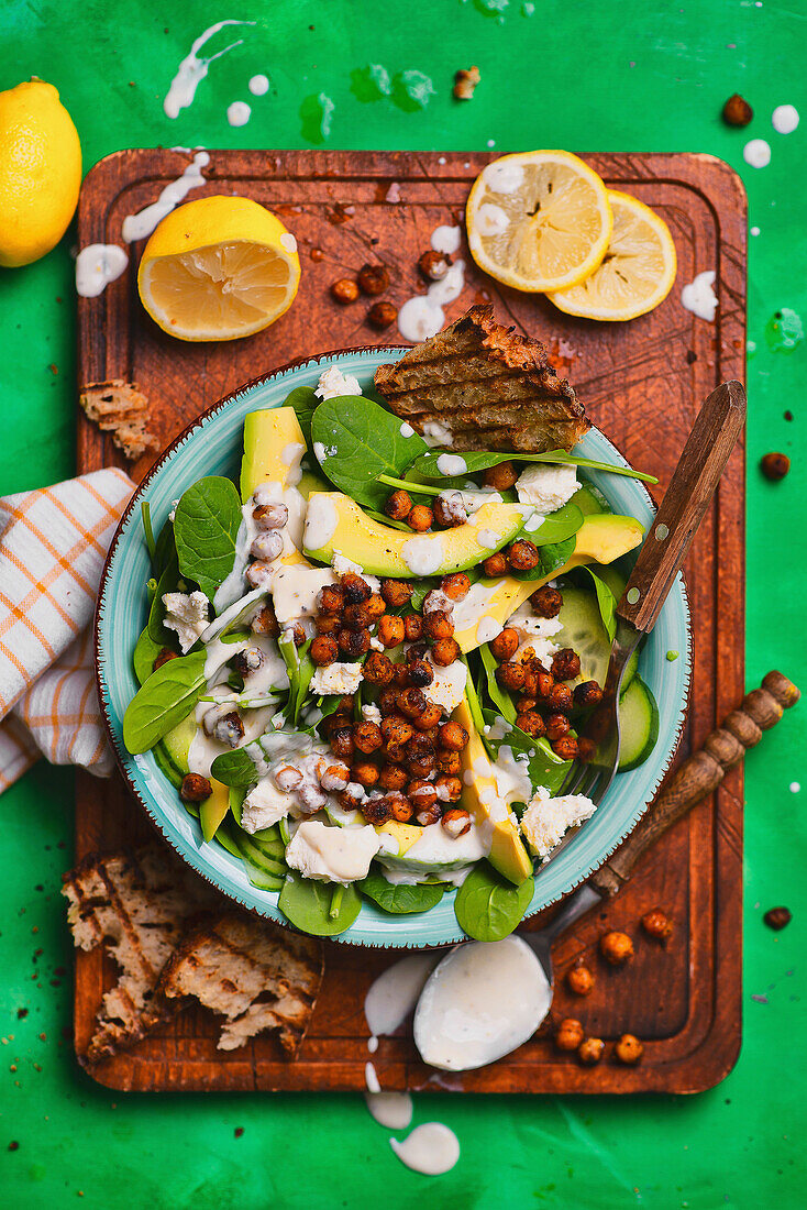 Spinach salad with avocado, cucumber, roasted chickpeas, and garlic dressing
