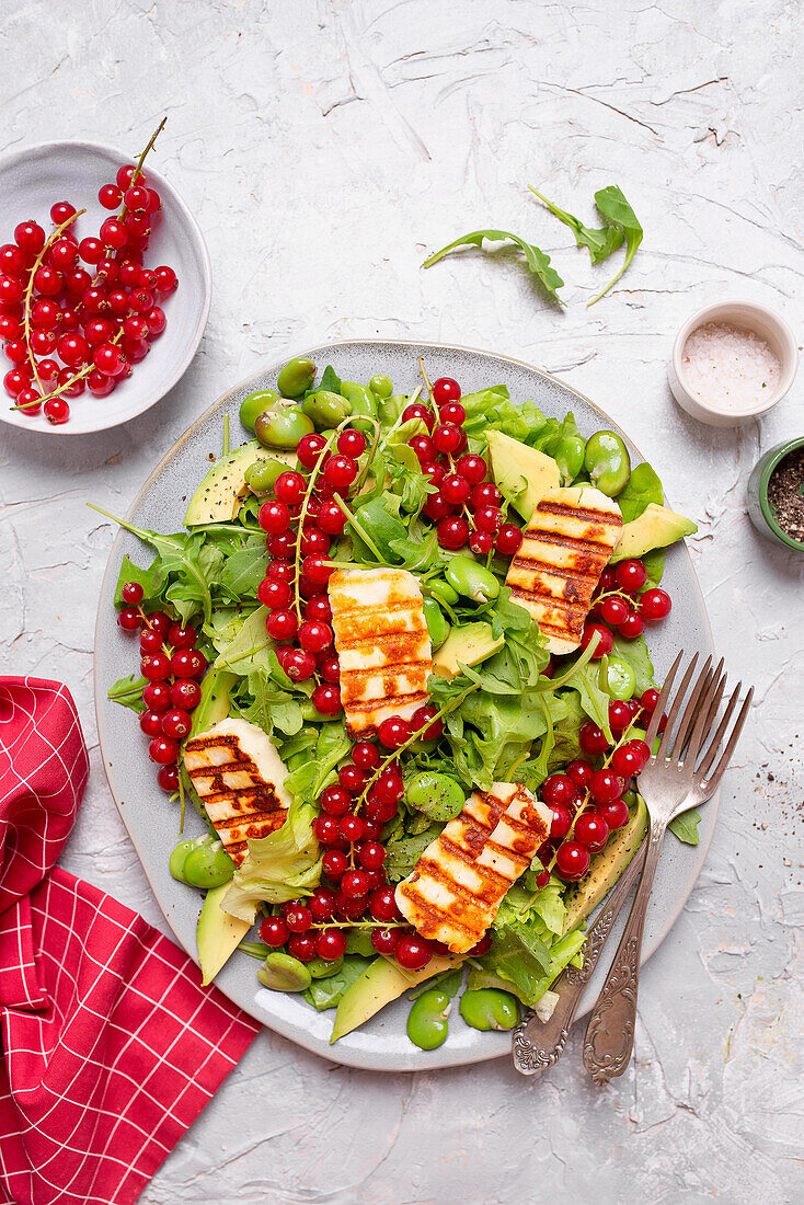 Salat mit Rucola, Avocado, Saubohnen, Halloumi und roten Johannisbeeren