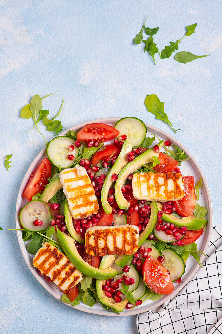 Salad with rocket, grilled halloumi, tomatoes, avocado, cucumber, and pomegranate seeds