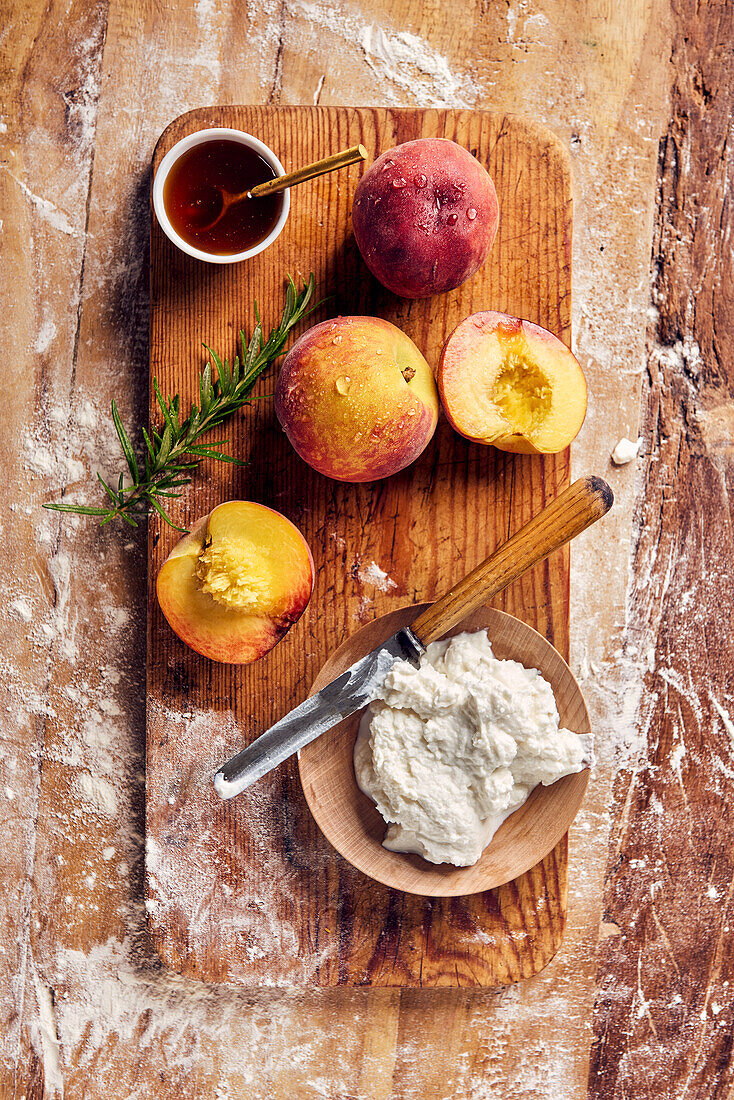 Peaches, ricotta in a wooden bowl, honey and rosemary on a wooden board