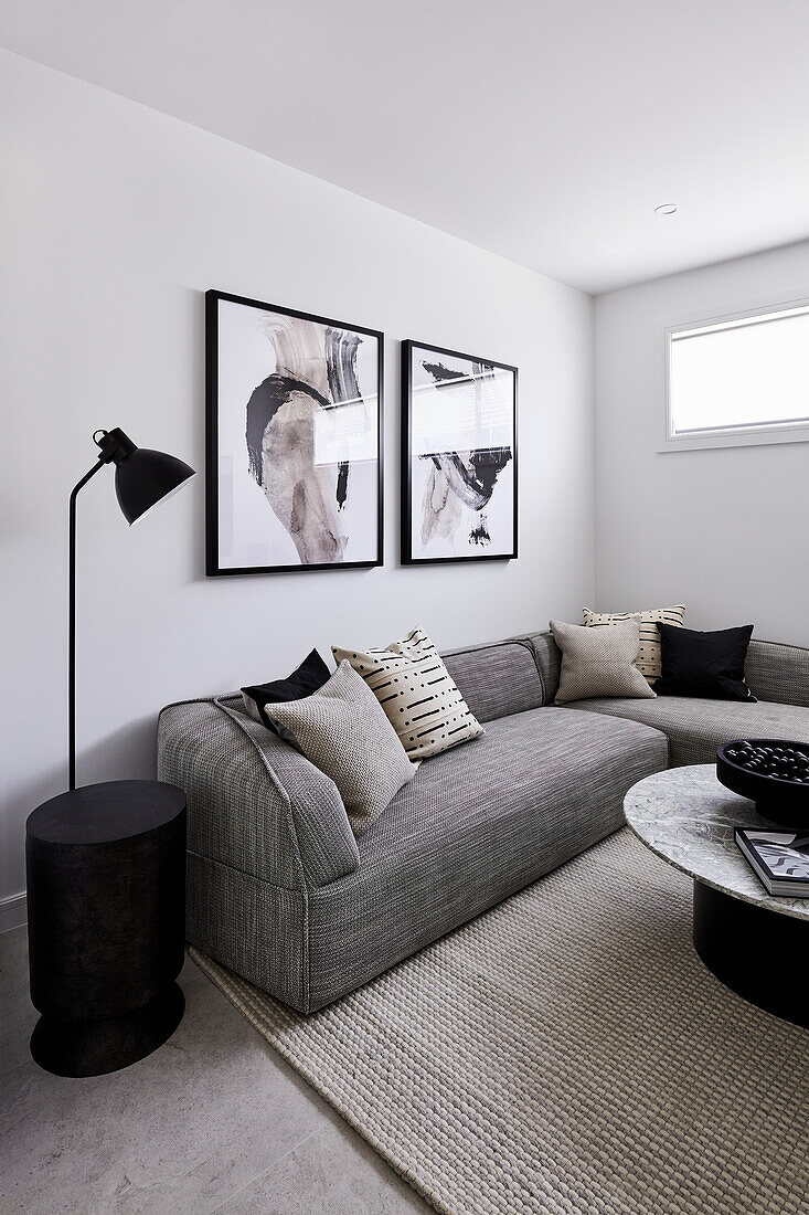 A modern monochromatic living room with a grey corner sofa, abstract artwork and marble coffee table