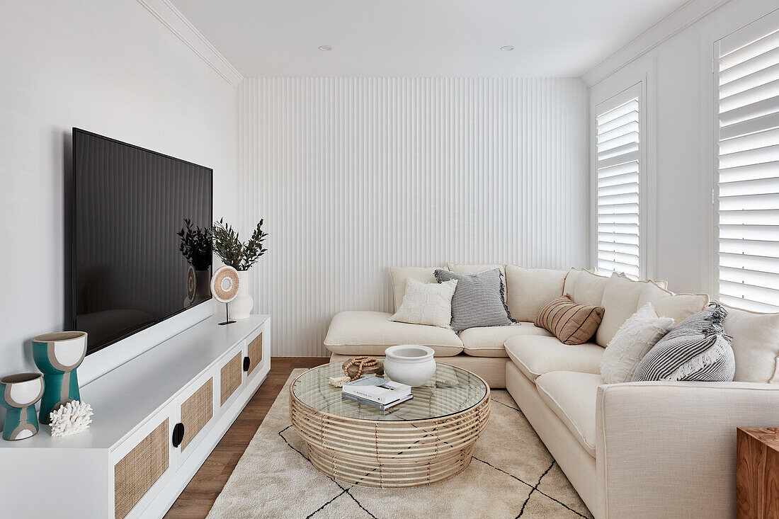 A modern coastal-style living room with a cream linen sofa, a fluted panel feature wall, plantation shutters and oak wood flooring