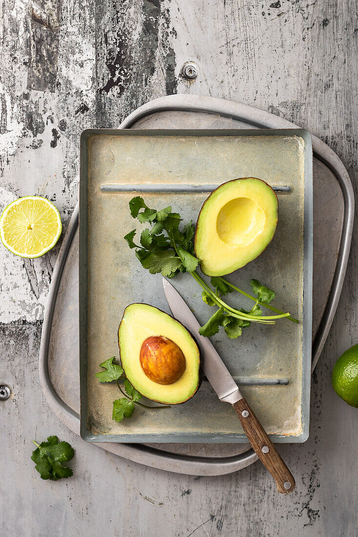 A halved avocado, fresh coriander and limes