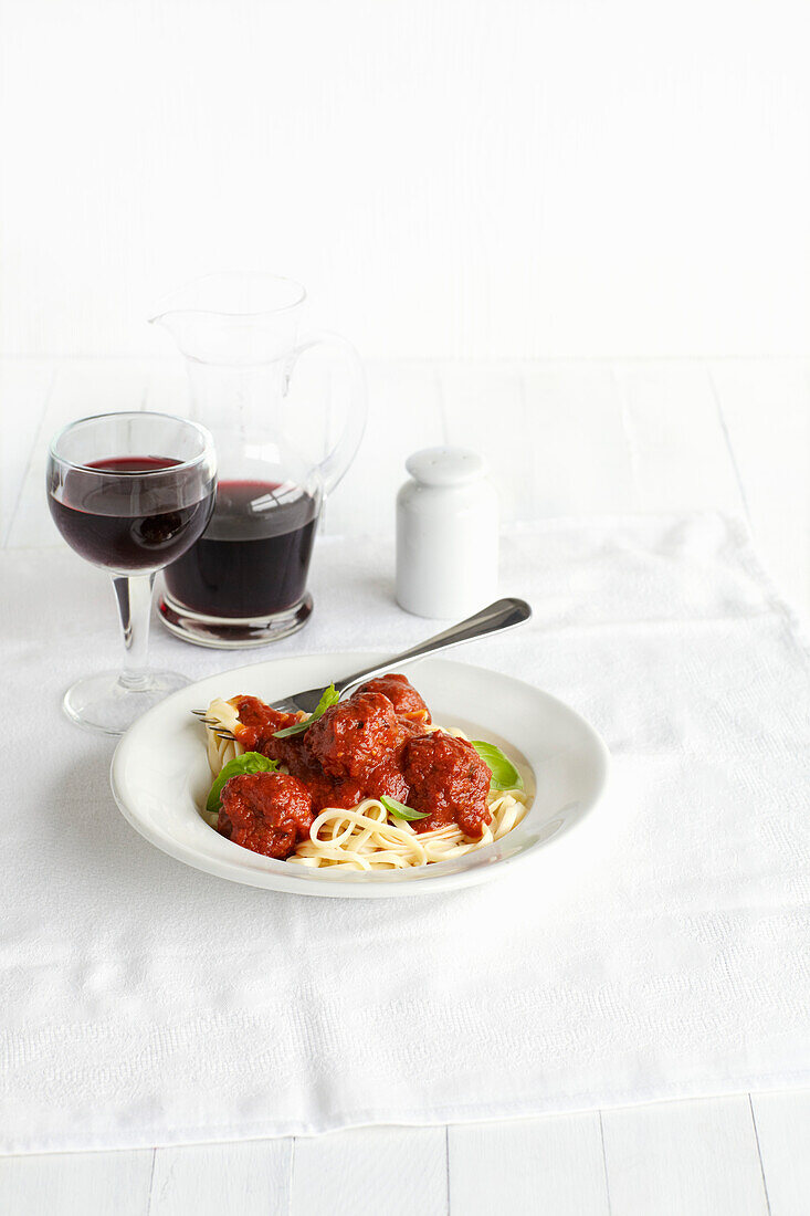 Kalbfleischbällchen mit geröstetem Tomatensugo auf Spaghetti dazu Rotwein in Glas und Karaffe