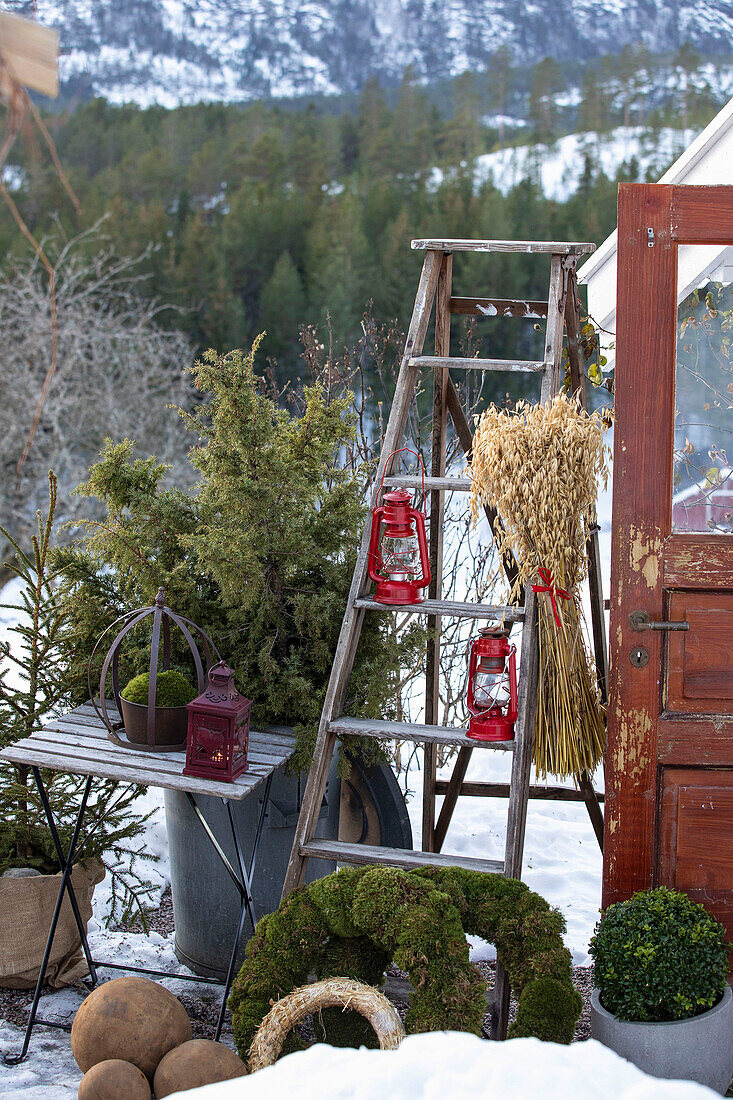 Kränze und Leiter mit Laterne auf winterlicher Terrasse