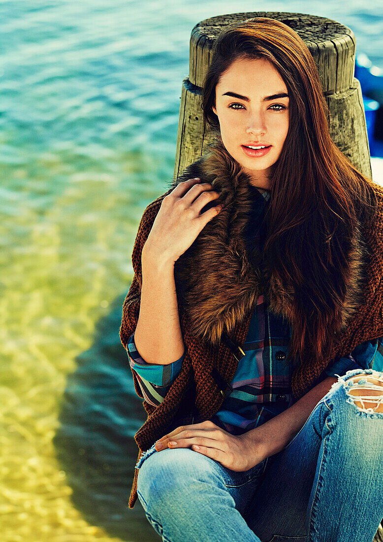 Junge brünette Frau in Strickjacke mit Fellkragen und Jeans am See