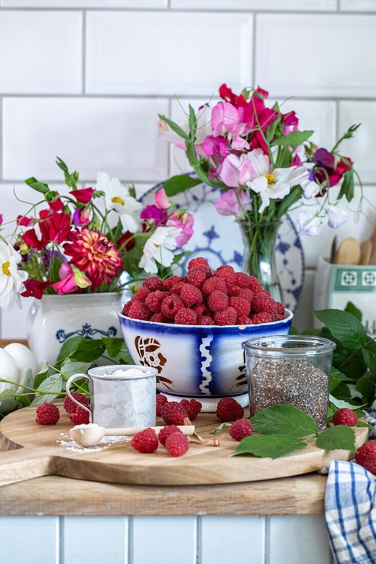 A bowl of raspberries and bouquets of flowers in a rural kitchen