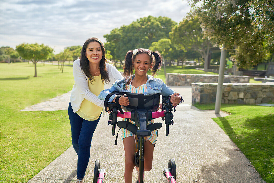 Happy mum and disabled daughter using a rollator in a park