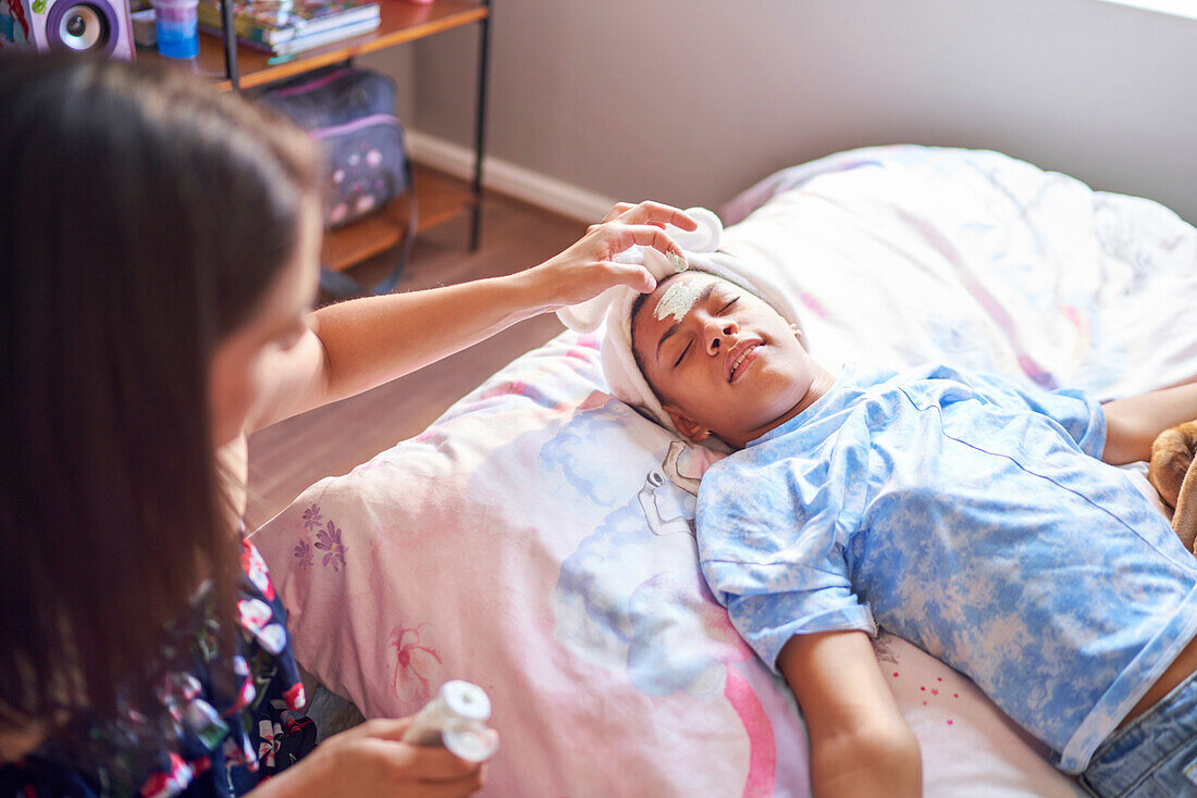 Mother giving disabled daughter a facial on bed at home