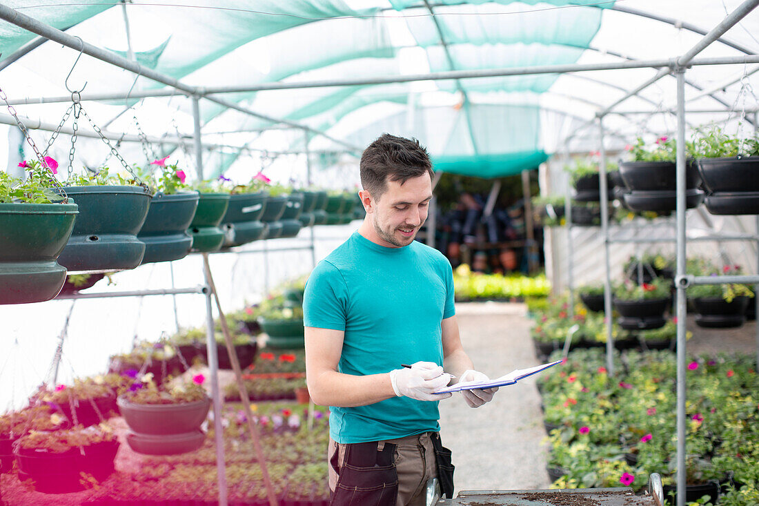 Male garden shop owner with clipboard in greenhouse