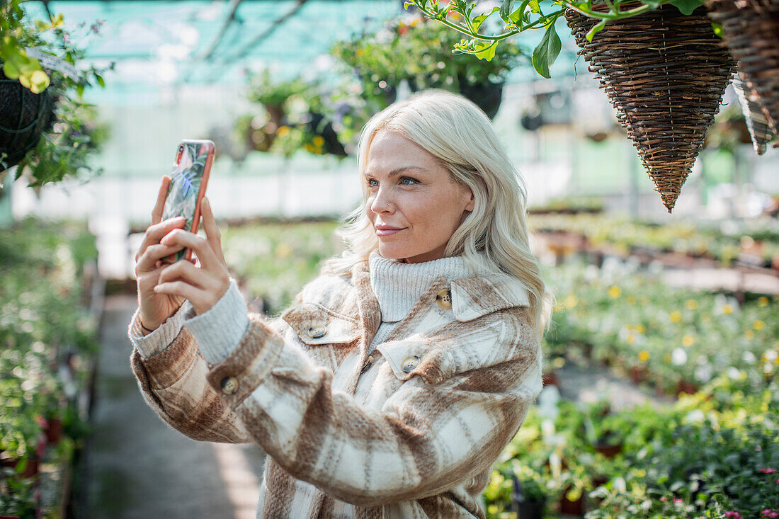 Woman with phone looking at hanging baskets in garden shop