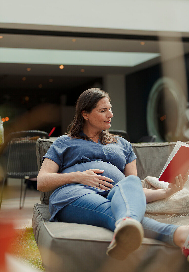 Pregnant woman reading book on patio lounge chair