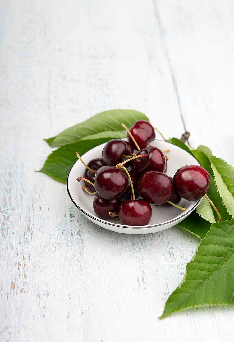 Fresh cherries in a shallow bowl next to leaves