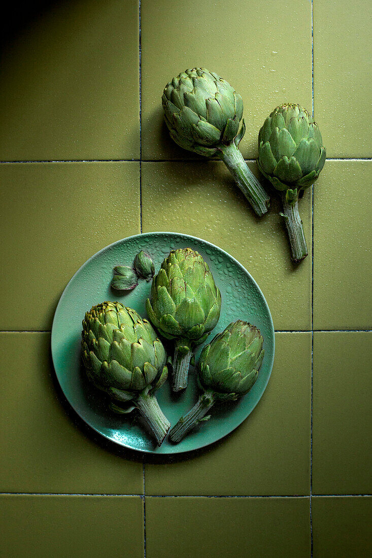 Artichokes on a green plate and green tile background