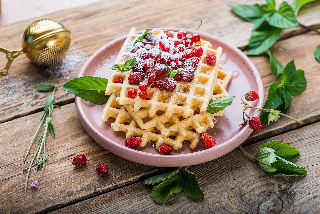 Waffles with wild strawberries, red currants, and confectionery sugar