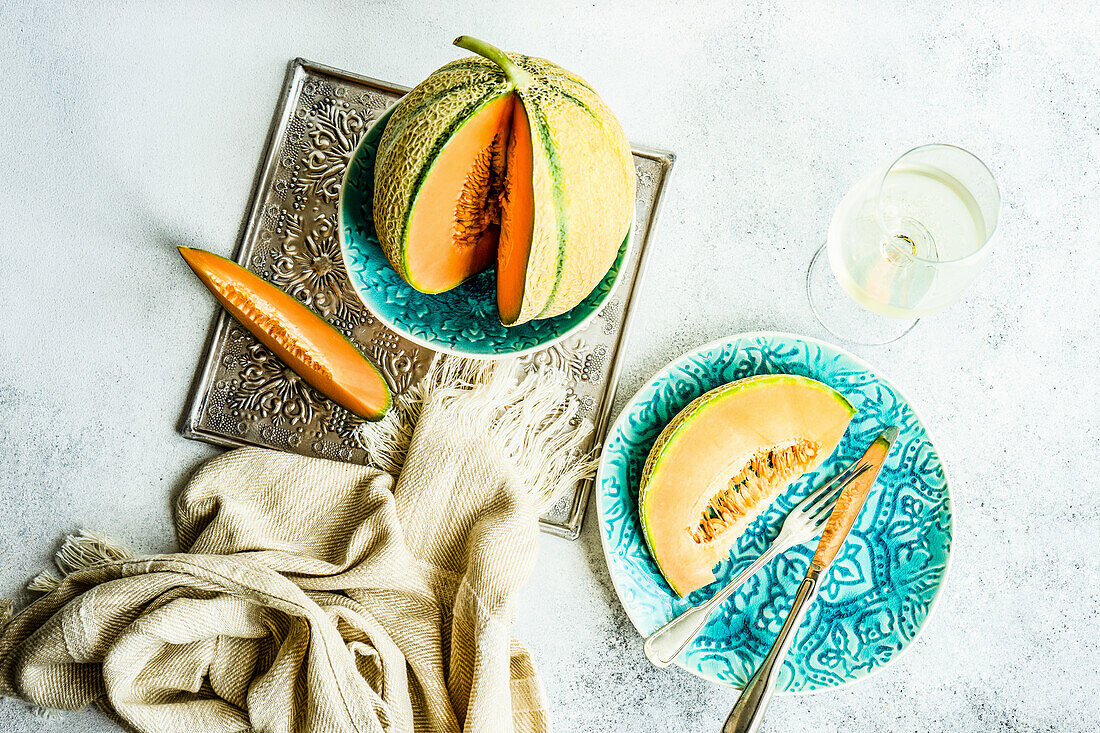 Ripe cantaloupe melon slices served on the ceramic plate with glass of cold white dry wine on concrete table