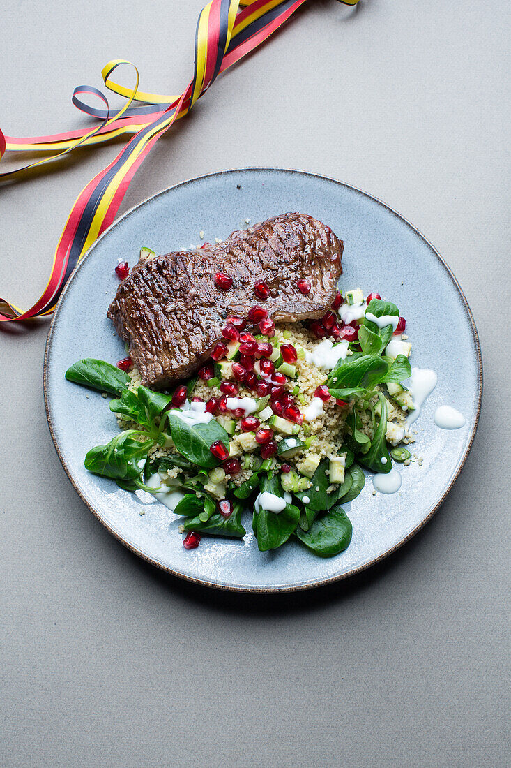 Steak served with couscous salad with lamb's lettuce, avocado, and pomegranate seeds