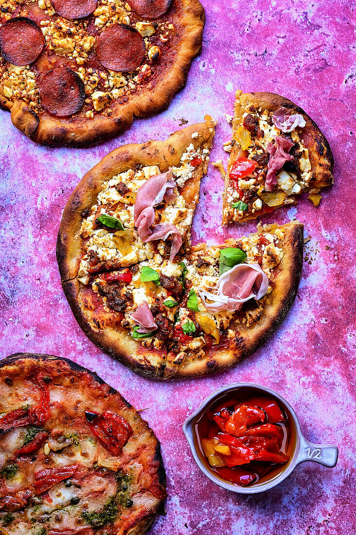 Different kinds of pizza with peppers, ham, and salami