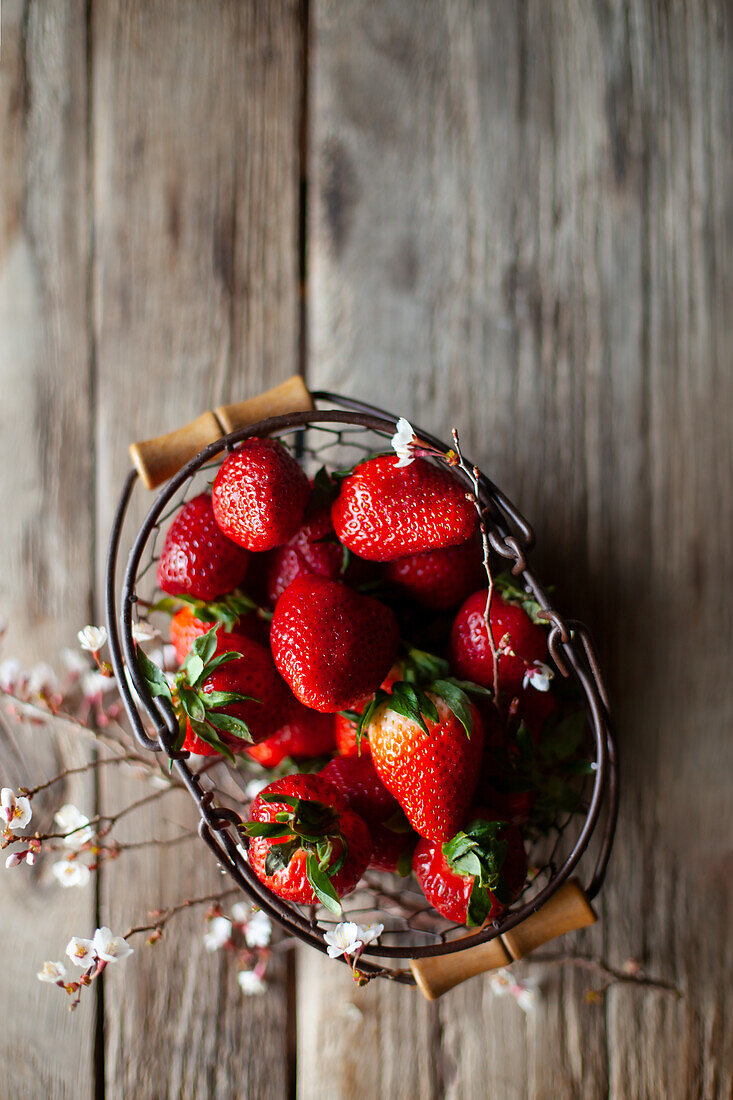 Frische Erdbeeren in Drahtkörbchen auf Holzuntergrund